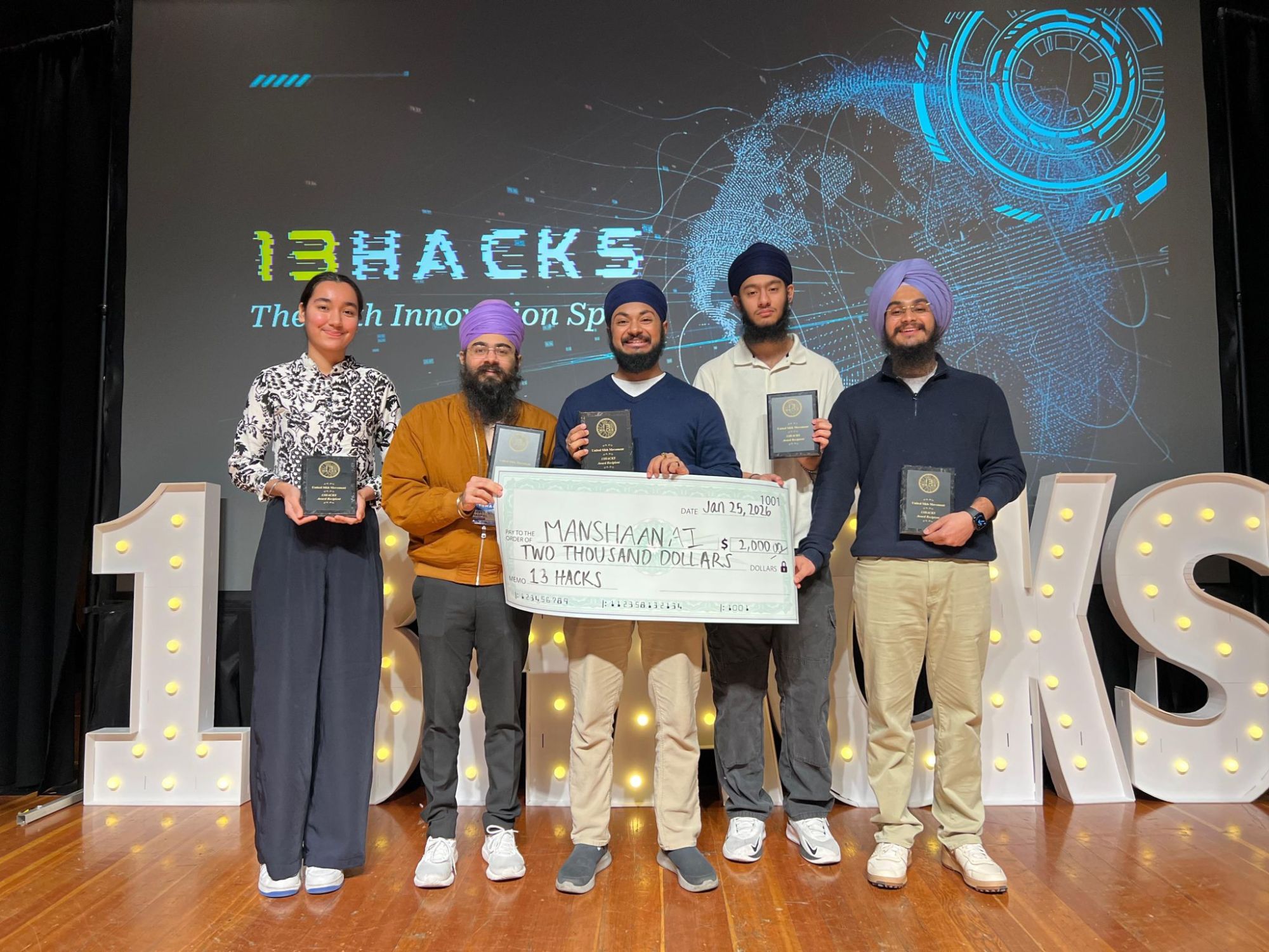Team Manshaan AI on stage at 13Hacks holding their award plaques and a $2,000 check